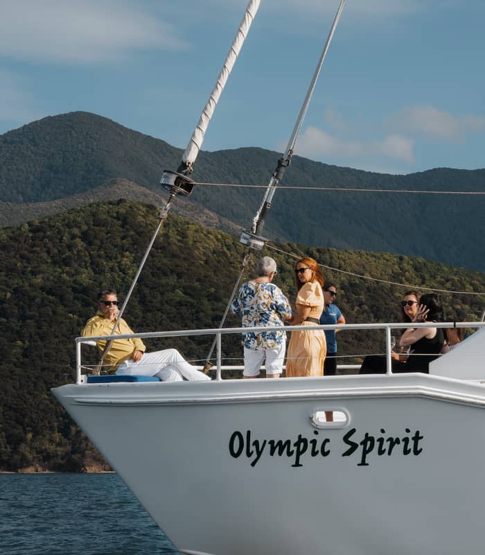 People on a sailboat named Olympic Spirit with mountains and water in the background on a sunny day.
