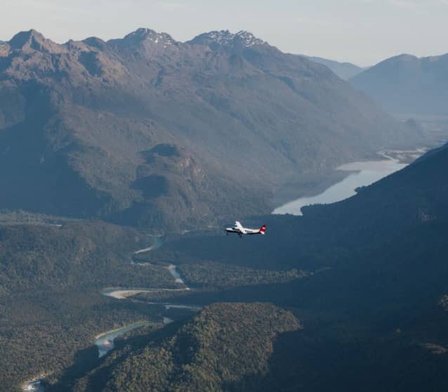 Small plane flying over green mountains and a winding river in Milford Sound.