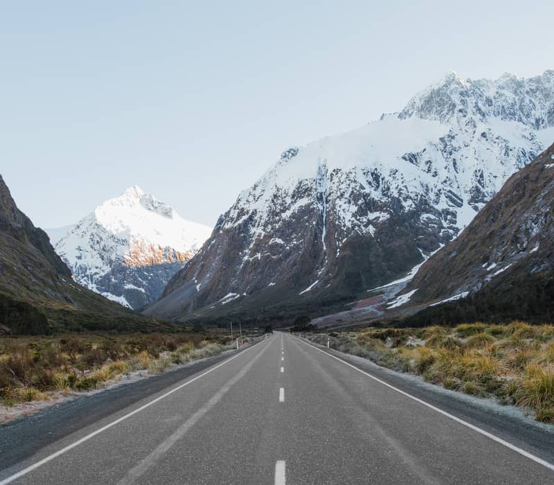 Road through valley with snowy mountains under clear sky