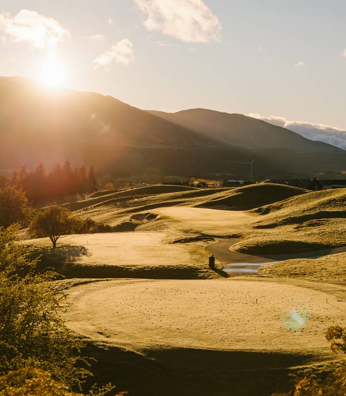Sunrise over a green golf course with hills and mountains in the background.