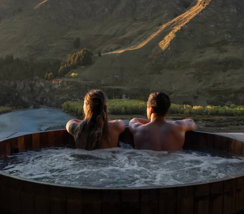 Couple in hot tub enjoying mountain view at sunset.