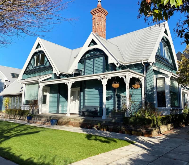 Blue Victorian house with white trim and green lawn on a sunny day