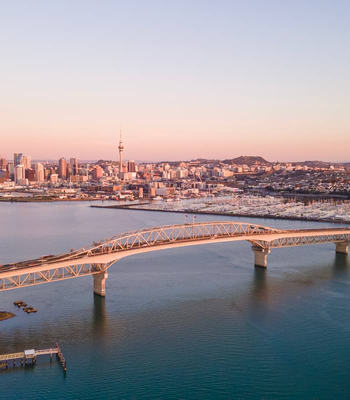Aerial view of Auckland city skyline with bridge and harbor at sunset.
