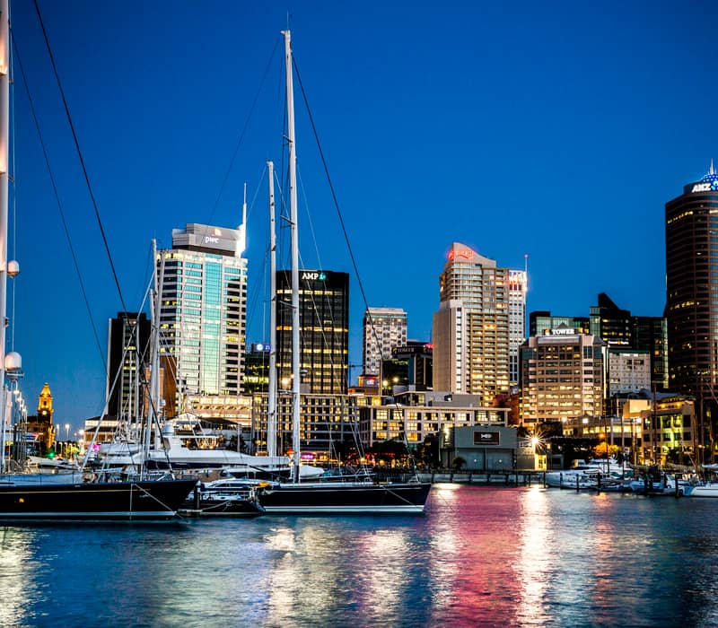 Auckland waterfront at night with boats docked and city lights reflecting on water.