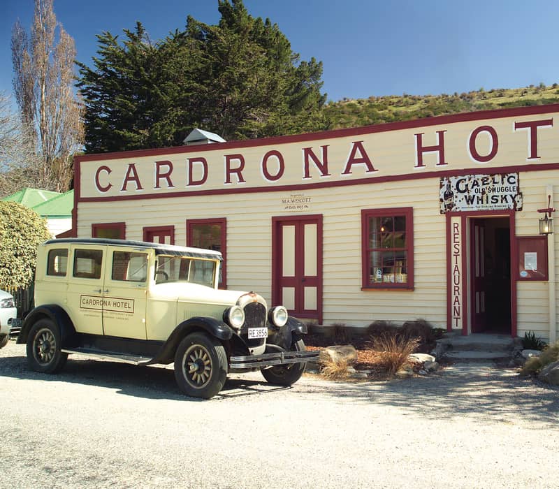 Historic Cardrona Hotel building with vintage car parked outside under clear sky.