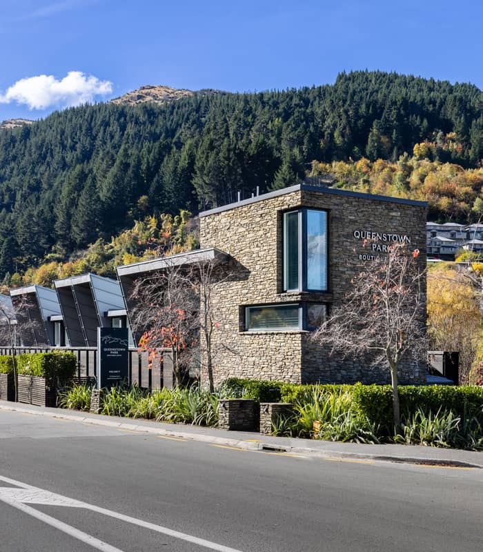 Stone building of Queenstown Park Boutique Hotel by a road with mountain and trees in background under blue sky