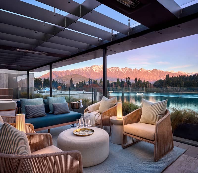Luxurious balcony seating with cushions overlooking lake and mountains at sunset.