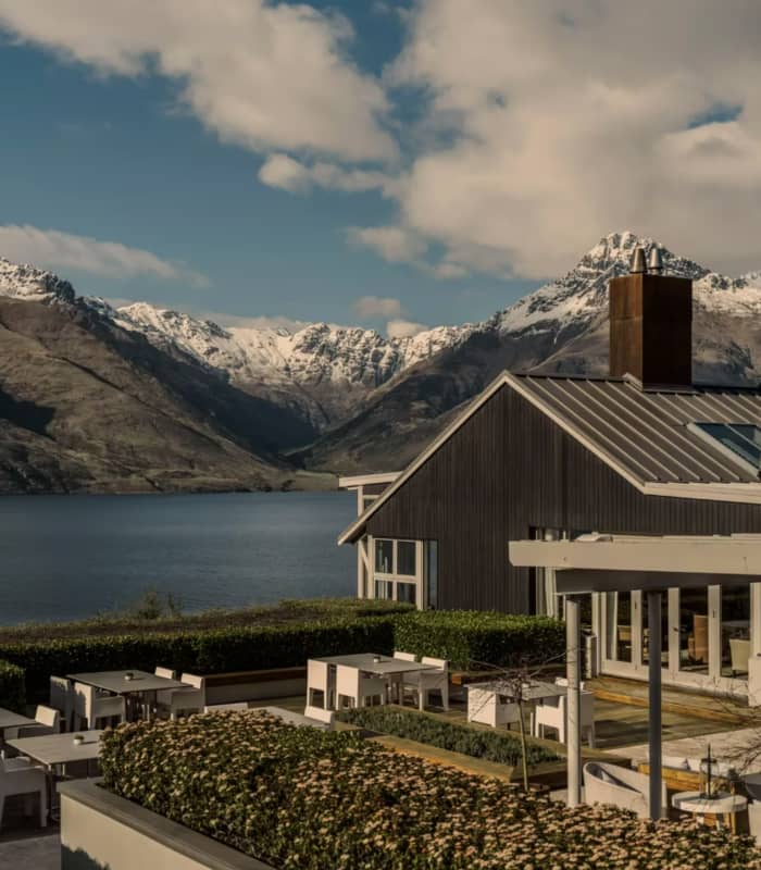 Outdoor terrace with tables by a lake, snow-covered mountains in the background.