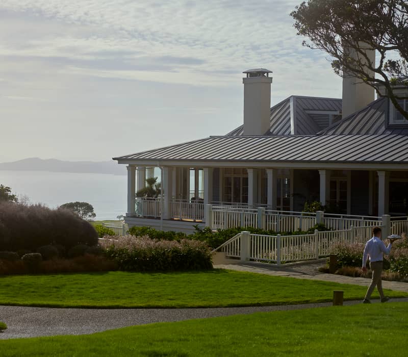 Exterior of a lodge with white columns, steps, and greenery in sunlight.