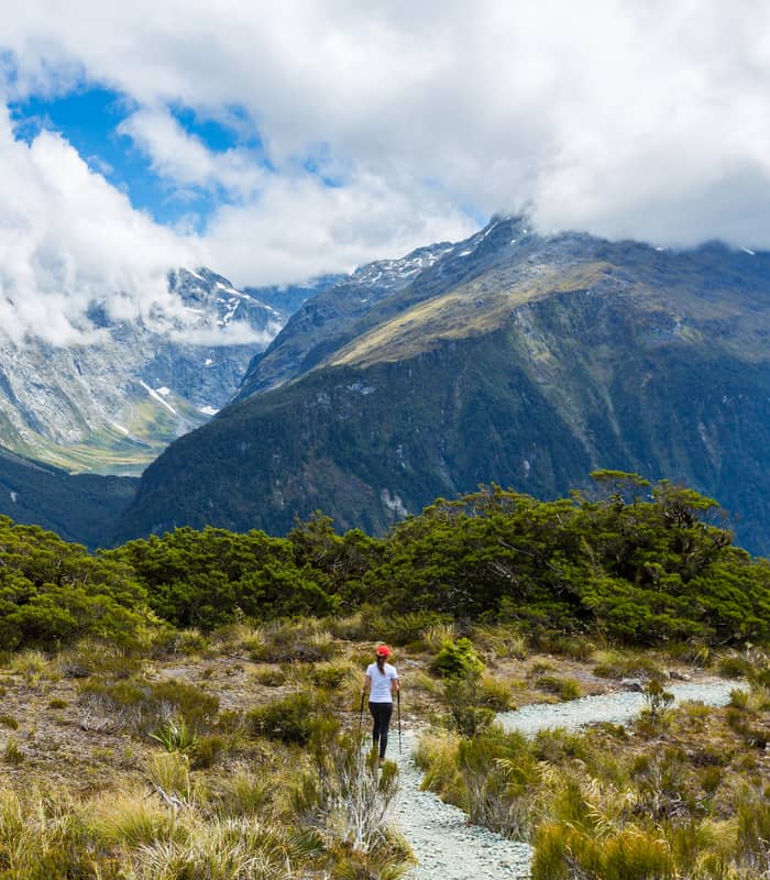 Hiker walking on a trail with mountains and clouds in the background