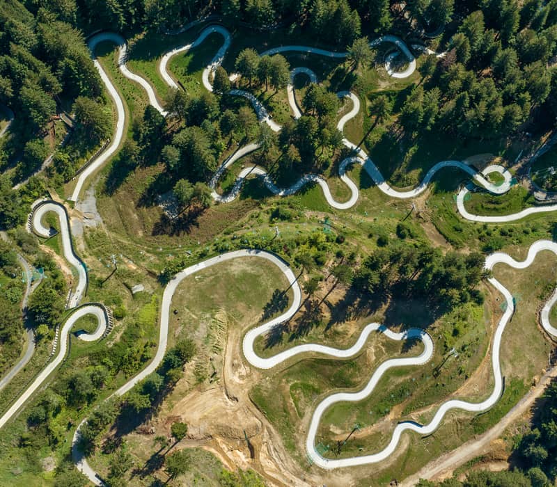 Aerial shot of winding luge tracks surrounded by forest and greenery on a hill.