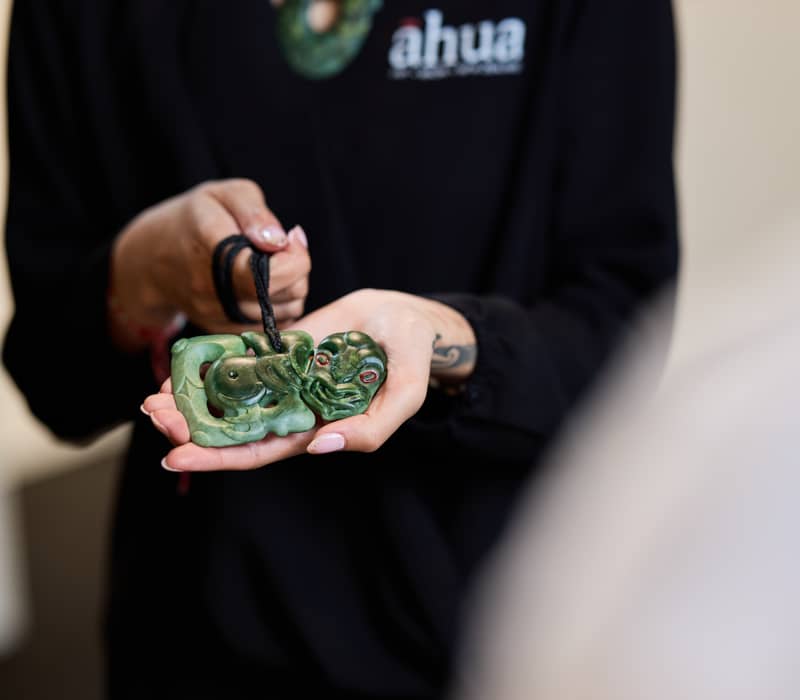 Hands hold a carved green jade pendant on a black rope.