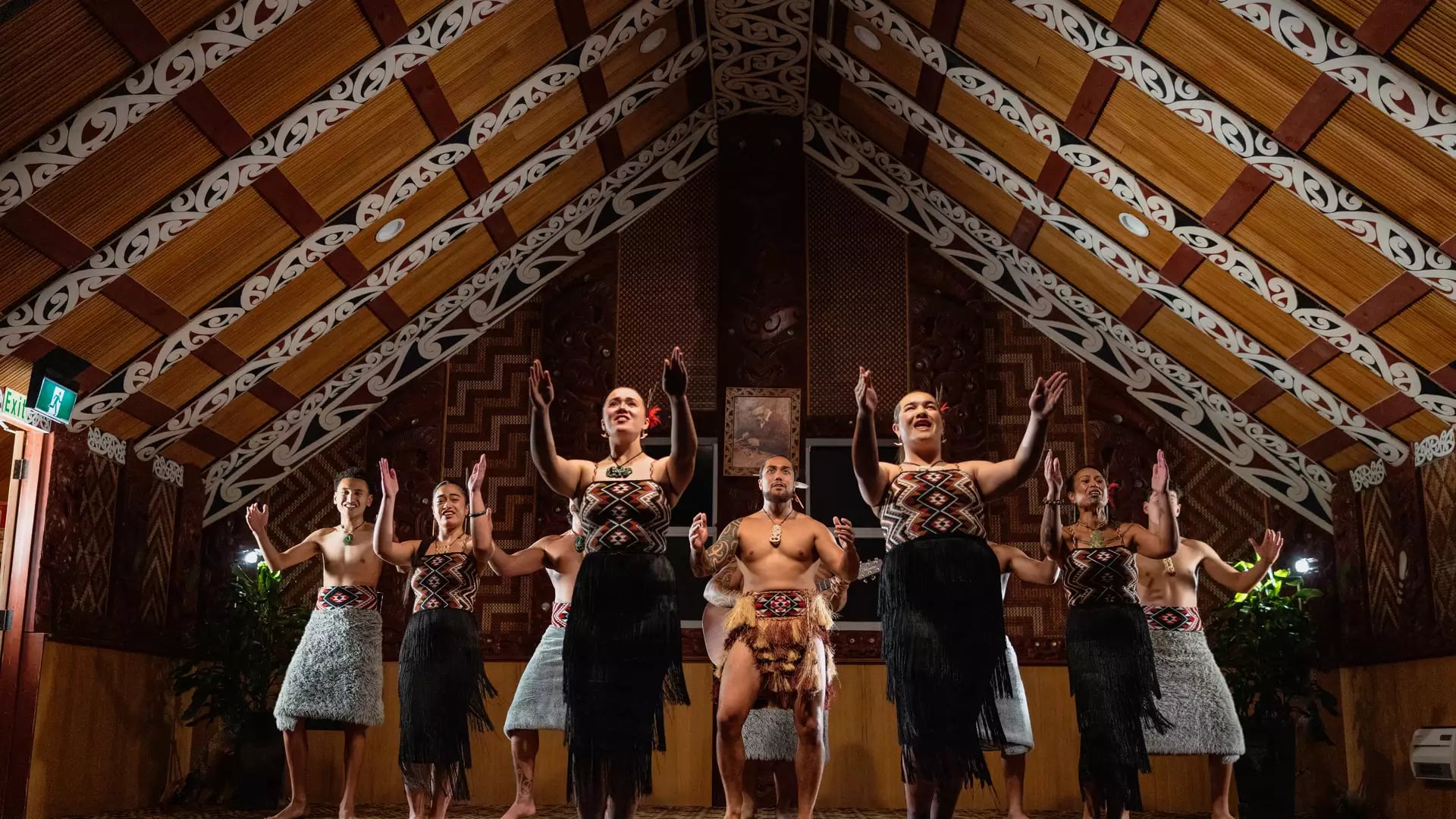Group performing traditional Maori dance inside ornately decorated meeting house