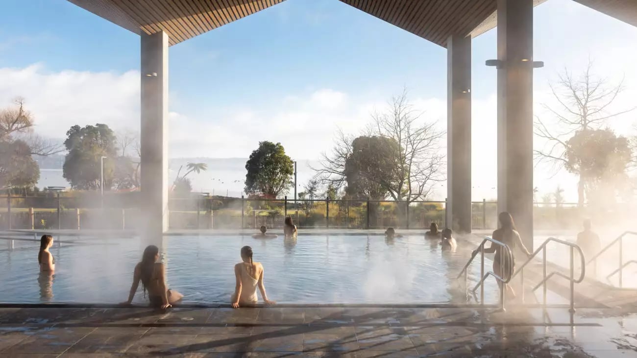 People relaxing in a steaming outdoor thermal pool with a lake and trees in the background.