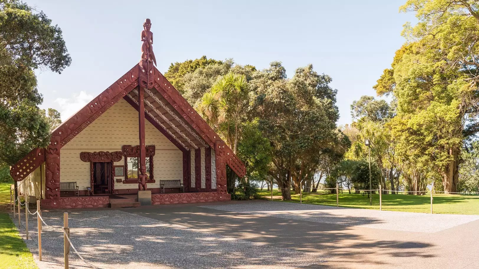 Traditional Maori meeting house with carvings at Waitangi Treaty Grounds near a lake and trees.