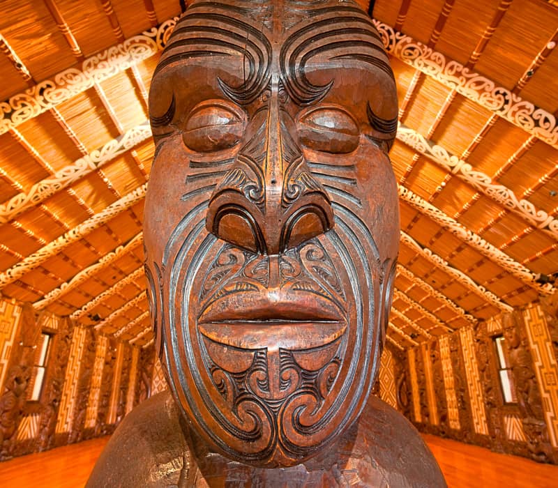 Close-up of a detailed Maori wood carving with tribal patterns inside an ornately decorated traditional building.