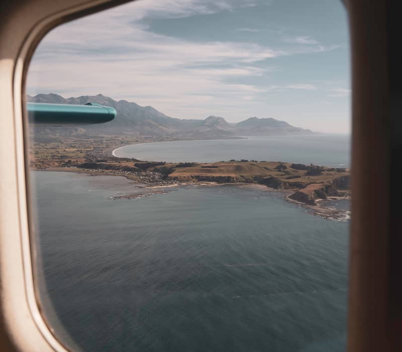 View of coastline and mountains through an airplane window over the ocean.