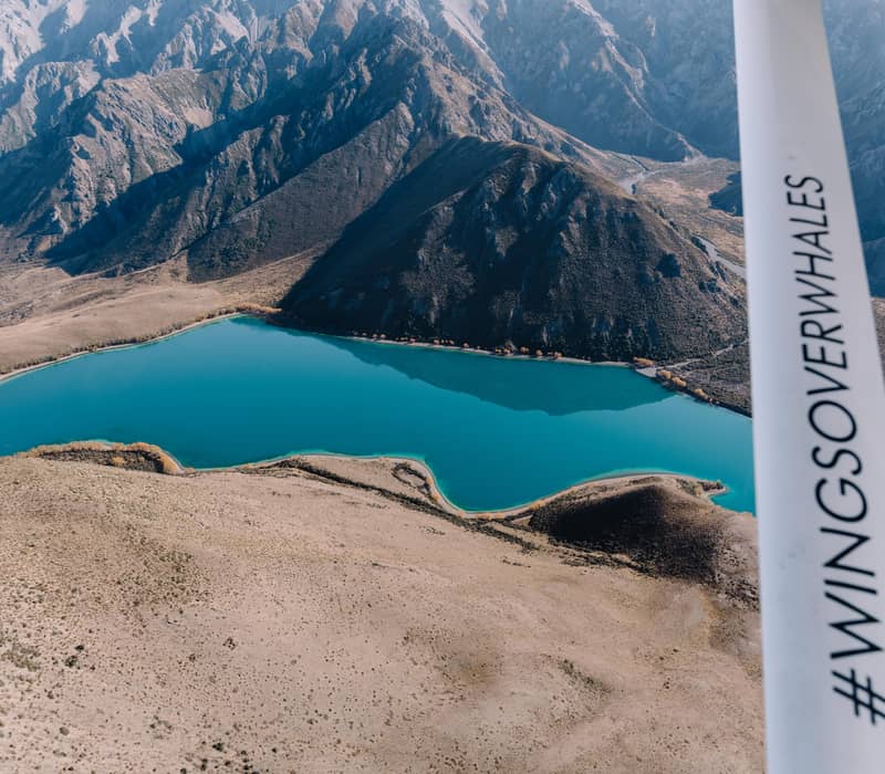 Aerial view of a turquoise lake surrounded by brown mountains and arid landscape from a plane.